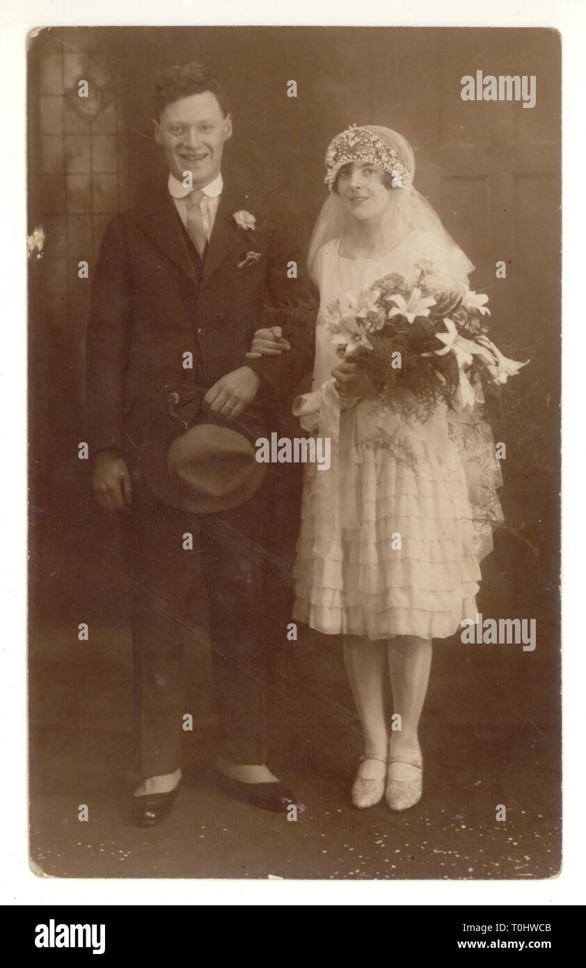 1920 Postkarte von Della und Jim's Hochzeit - ein sehr stilvolles Paar. Della hat den modischen höhere Saum. - Ein 'Flapper Girl' mit Kopftuch und langen Schleier. Jim trägt Gamaschen über seine Schuhe. Vom 1926 auf der Rückseite, Großbritannien Stockfoto