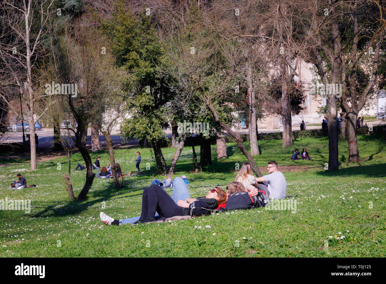 Rom, Italien, 3. März 2019: In der öffentlichen Park der Villa Borghese, einige Jungen liegen auf dem Gras in einen Moment der Entspannung. Ein Junge und ein Mädchen sonnen. Auf Stockfoto