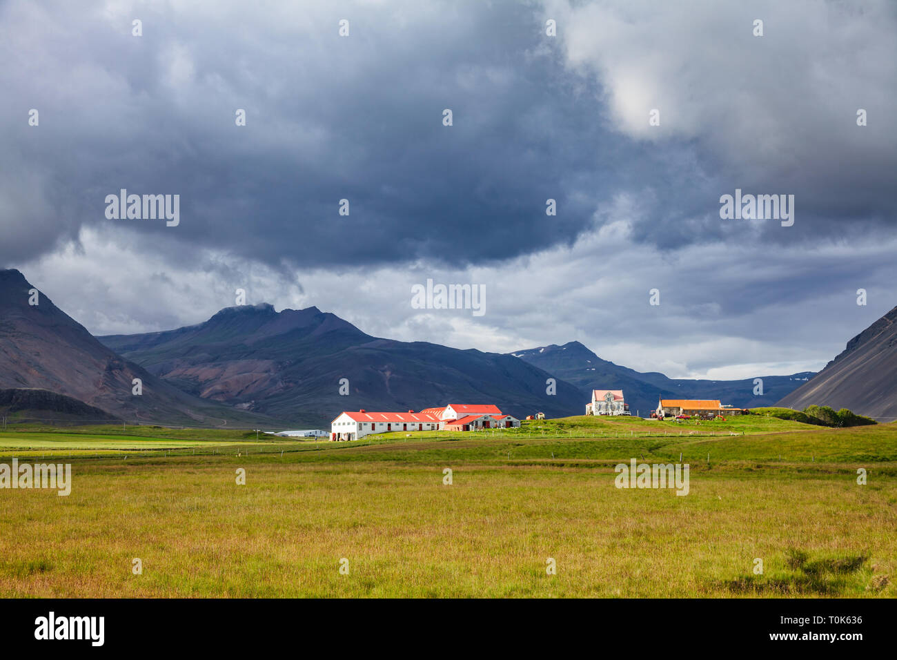 Isländische Landschaft mit Bauernhof Häuser unter düsteren Himmel am Fuße des vulkanischen Berge - rauhe landwirtschaftlichen conitions Konzept, Ost Island, Stockfoto