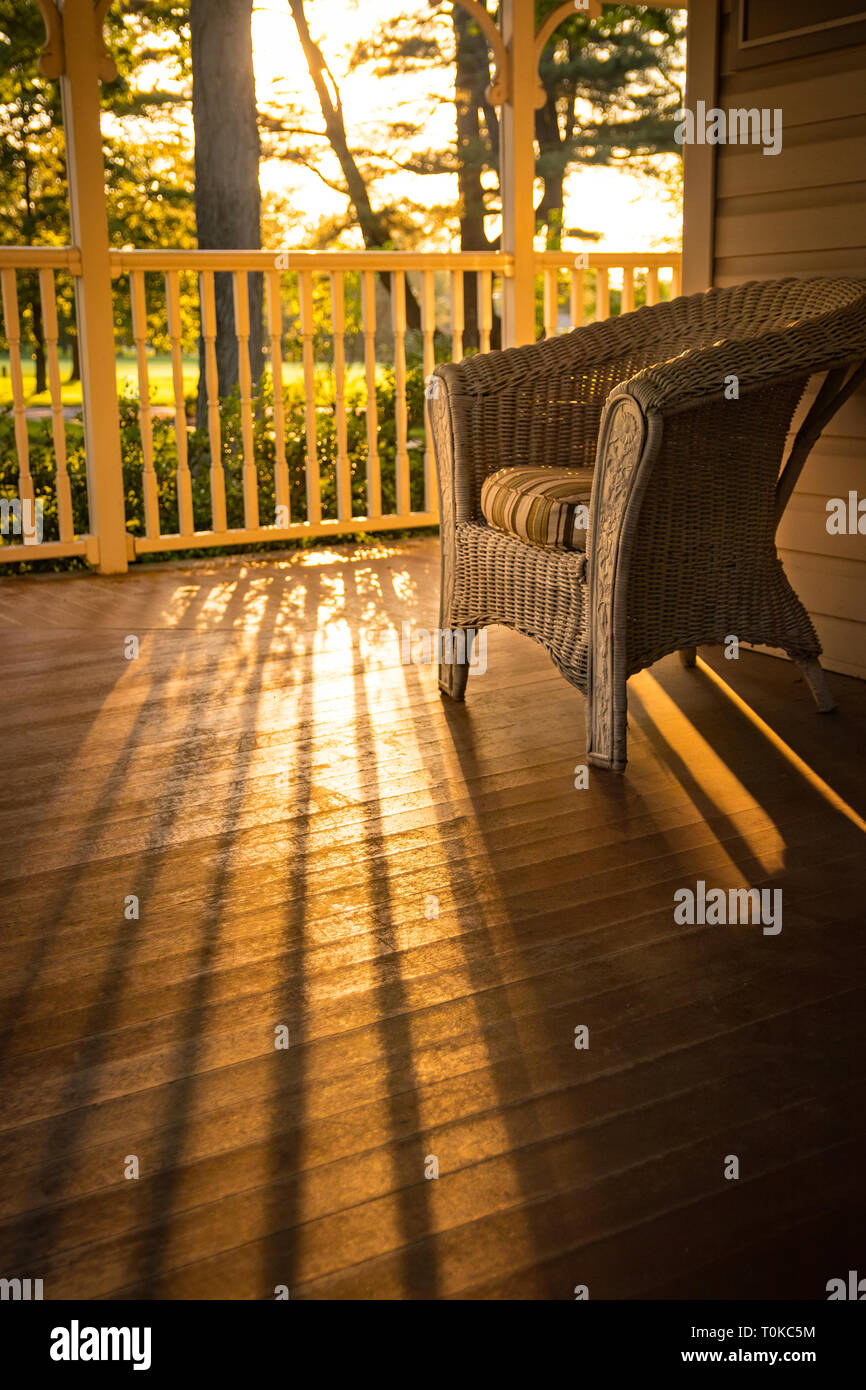 Warme, sonnige Aussicht von zu Hause: einen Korbstuhl auf hölzernen Veranda. Stockfoto