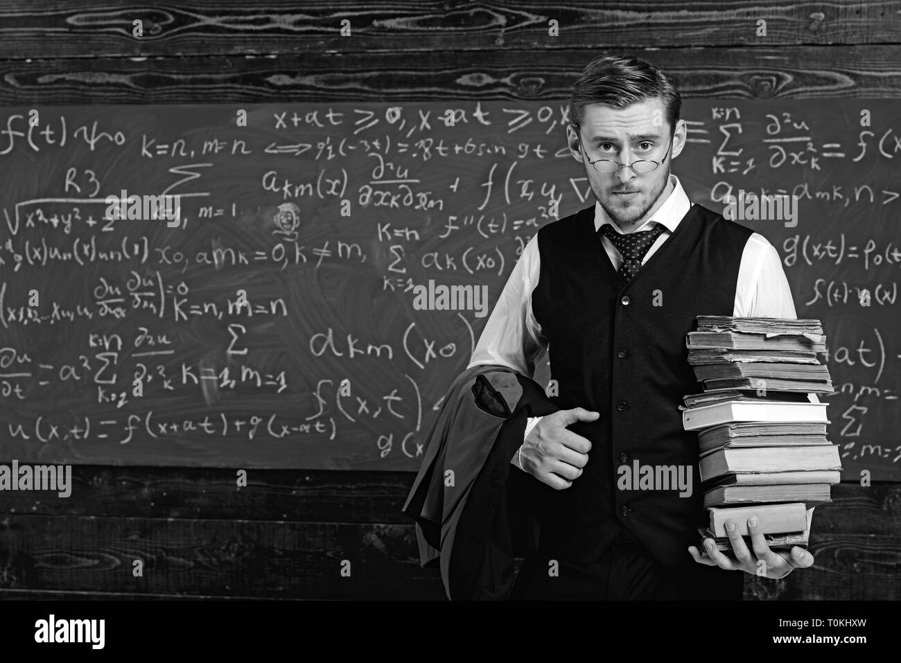 Junger Student in Anzug und Brille zu Fuß zu Bibliothek mit Haufen Bücher. Bücherwurm studieren für Prüfung Stockfoto