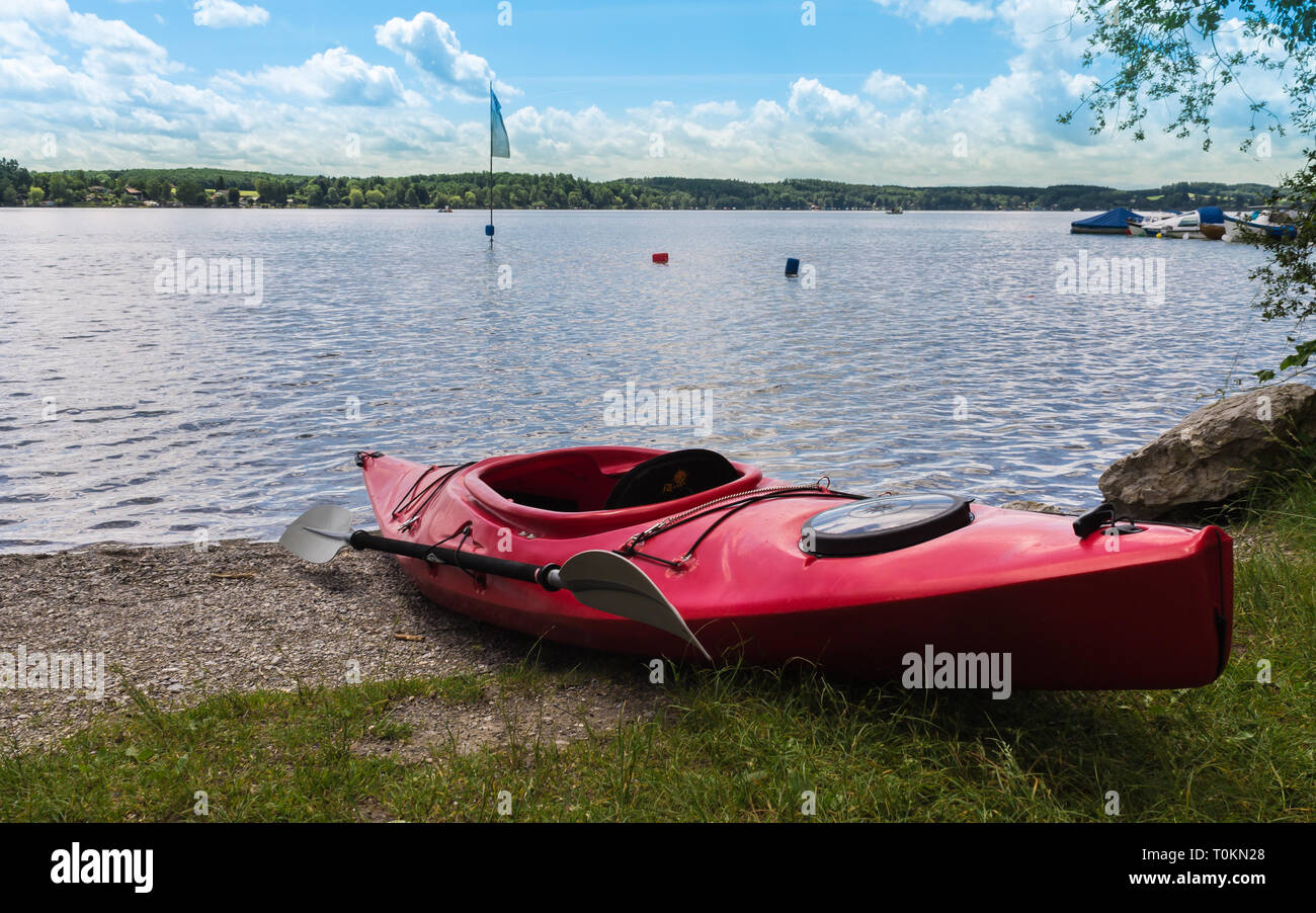 Rotes Wasser reisen Kajak liegen auf dem Strand von Wörthsee. Im  Hintergrund die See mit Flagge, Boote und Pier in Wörthsee, Bayern,  Deutschland, Europa Stockfotografie - Alamy