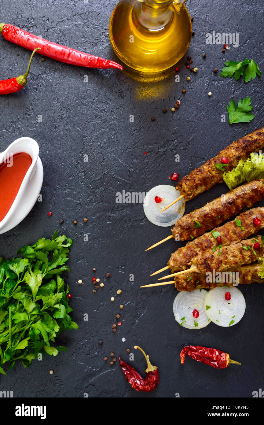 Lula Kebab ist eine traditionelle arabische Gericht. Fleisch Schaschlik auf Holzspieße, würzigen Tomatensauce auf schwarzem Hintergrund. Die Draufsicht, spase kopieren Stockfoto