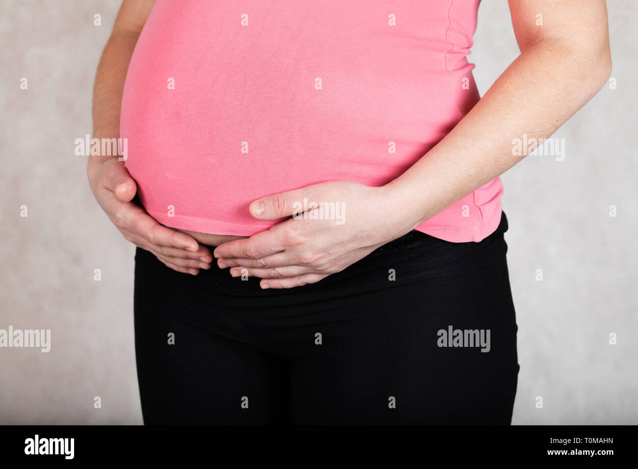 Junge schwangere zwischen 30 und 35 Jahre alte Frau hält ihre Hände auf den Bauch. Nahaufnahme Stockfoto