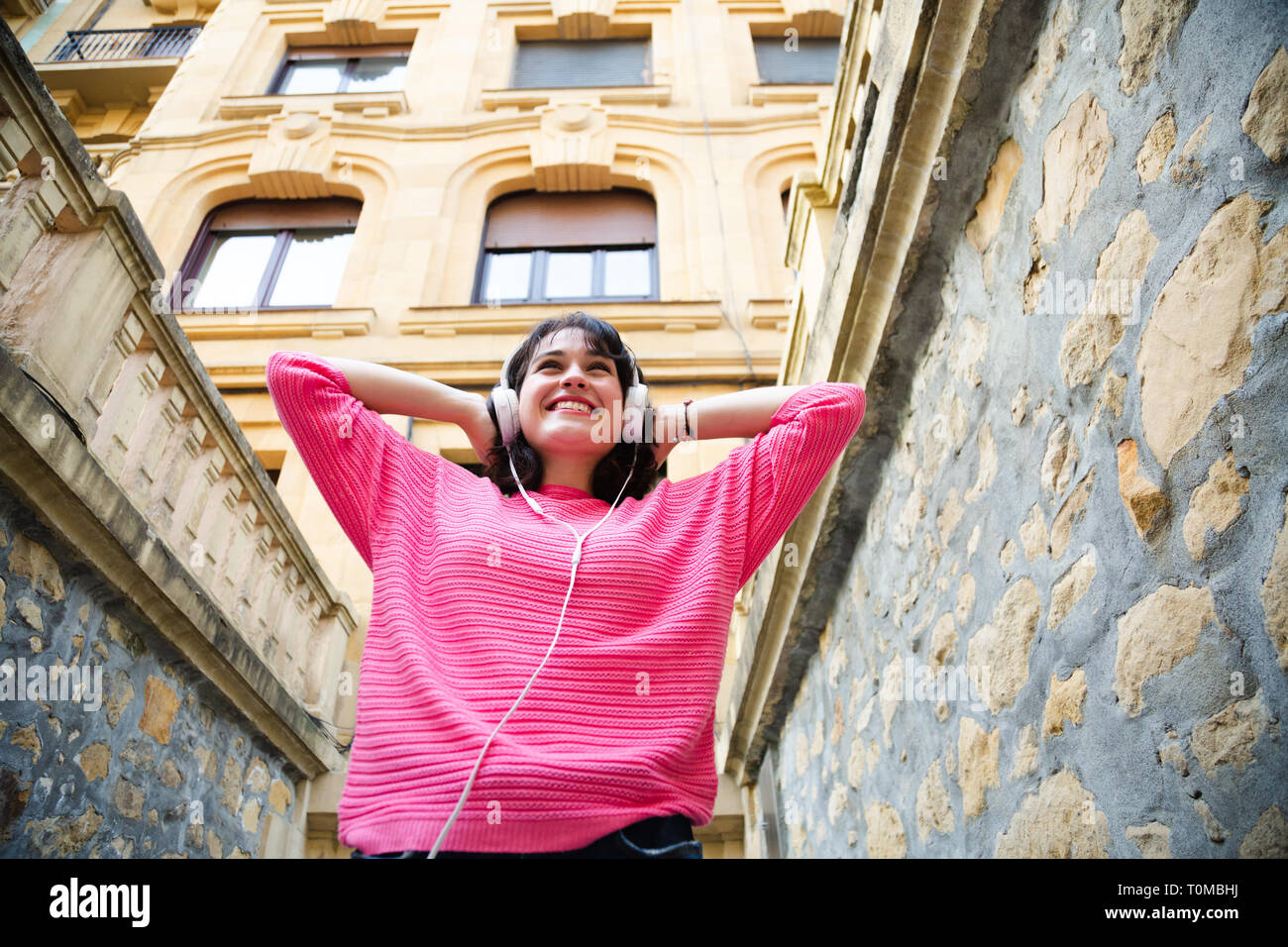 Glückliche junge Frau in rosa Pullover das Hören von Musik in der Straße. Low Angle View Stockfoto