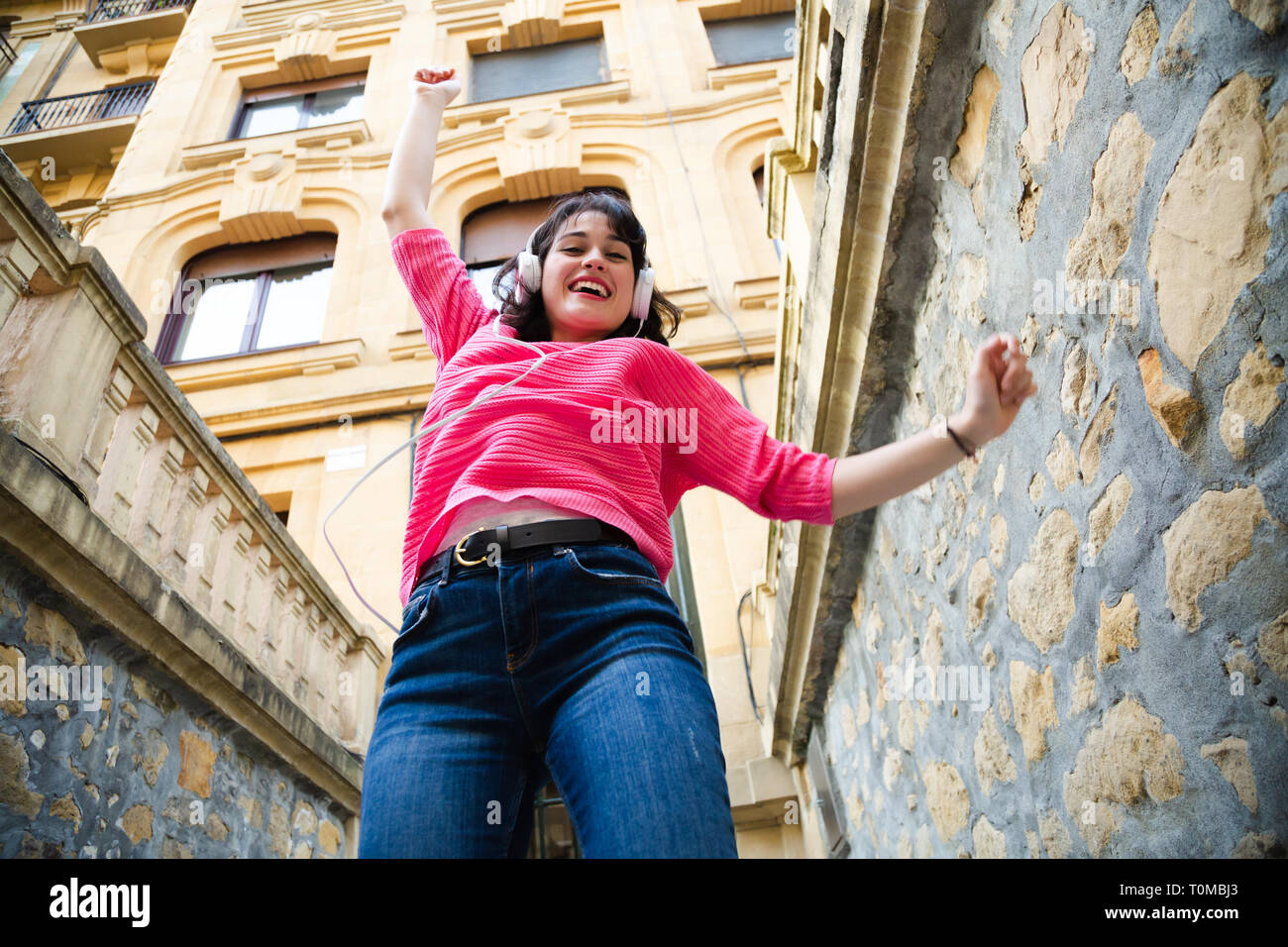 Glückliche junge Frau in rosa Pullover Musik hören und tanzen auf der Straße. Low Angle View Stockfoto