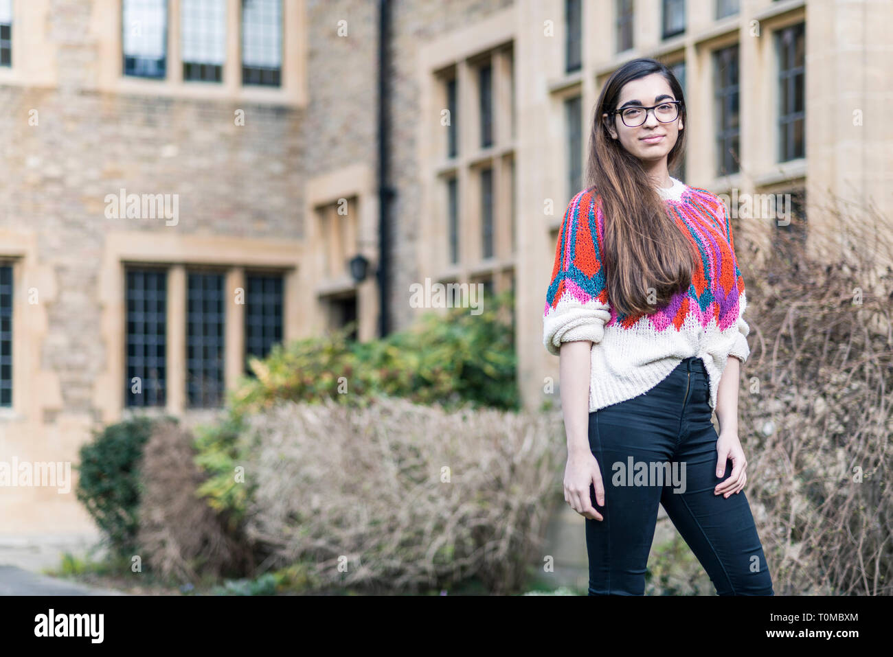 Eine junge International Student steht auf dem Campus Gelände eines Cambridge College von traditionellen historischen Gebäuden umgeben Stockfoto