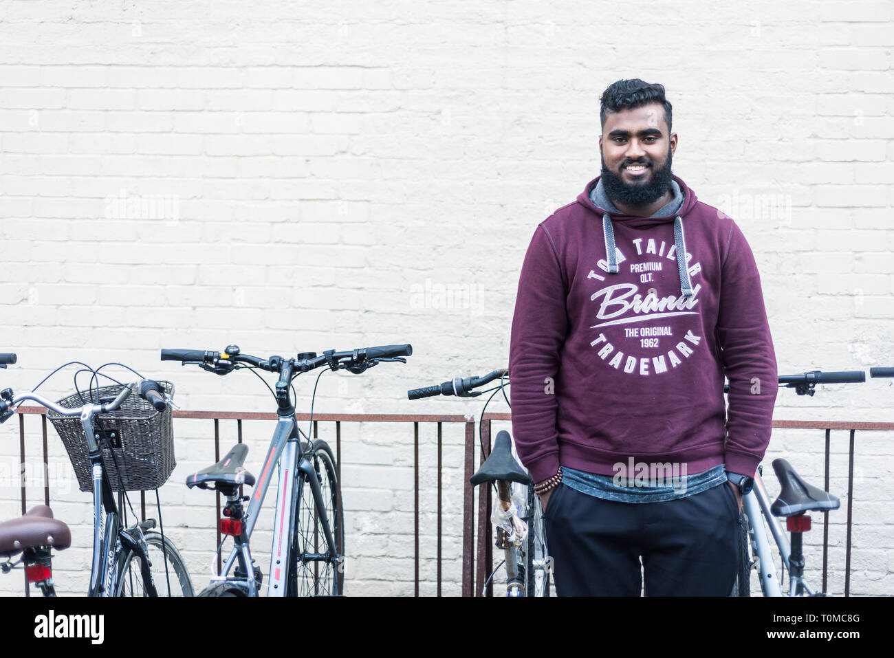 Ein männlicher Internationale asiatische Studentin aus dem indischen Subkontinent, sitzt unter den Fahrrad-/Zyklus Lagerung in einem Cambridge College Stockfoto
