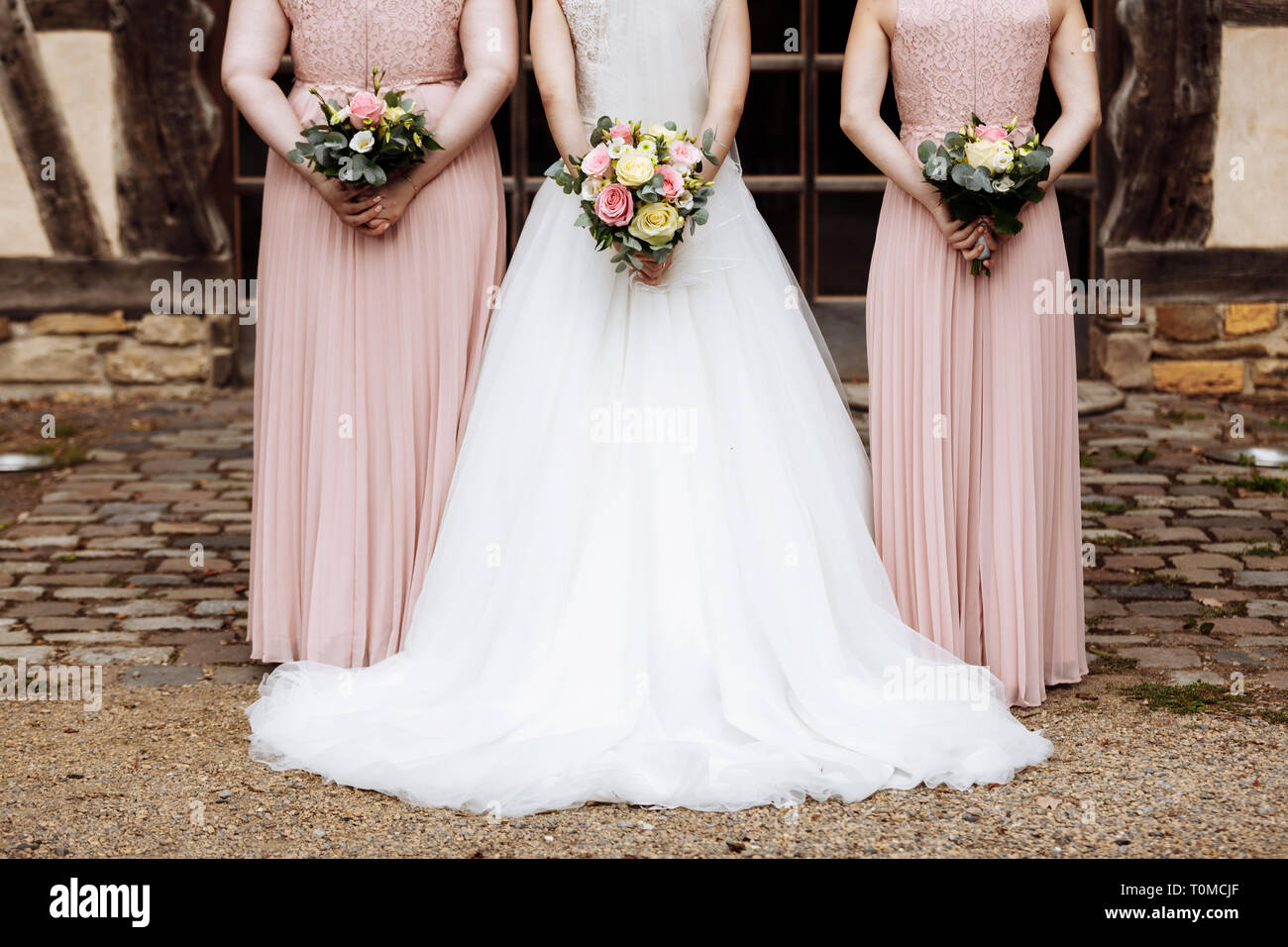 Die Braut und Brautjungfern in einem eleganten Kleid steht und die hand  Blumensträuße von Pastell rosa Blumen und Grün mit Schleife an der Natur.  Junge bea Stockfotografie - Alamy