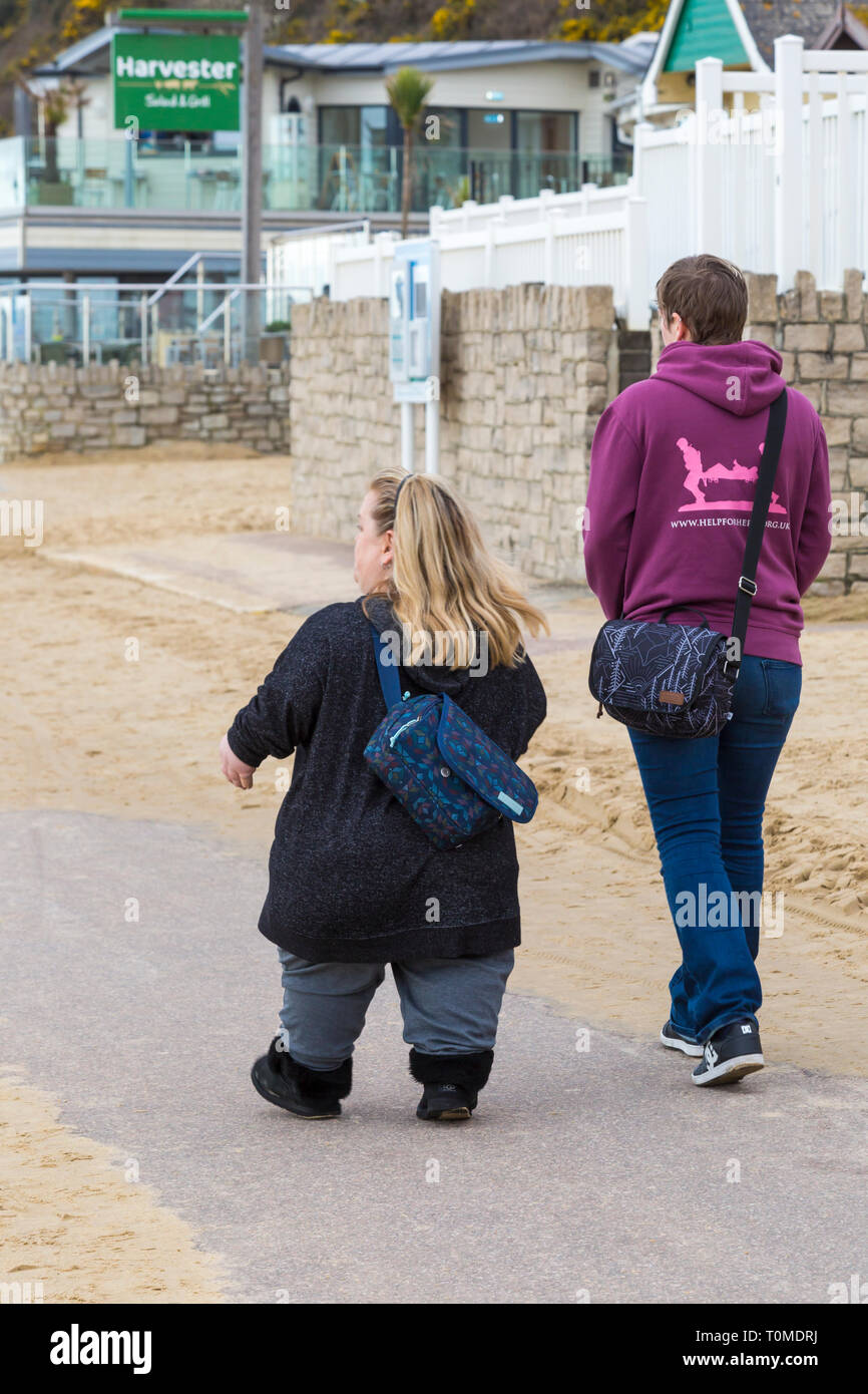 Zwei Frauen, eine von Kleinwuchs, Wandern entlang der Promenade an der Durley Chine, West Underfcliff Promenade, Bournemouth, Dorset UK im März Stockfoto
