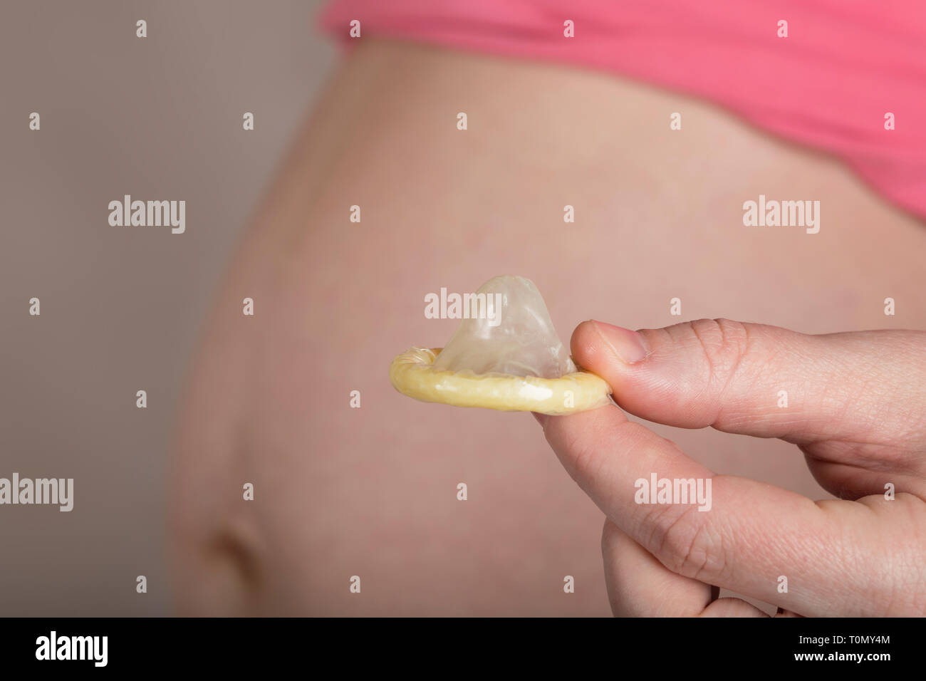 Junge schwangere zwischen 30 und 35 Jahre alte Frau hält ein Kondom nah an ihren Bauch. Nahaufnahme Stockfoto