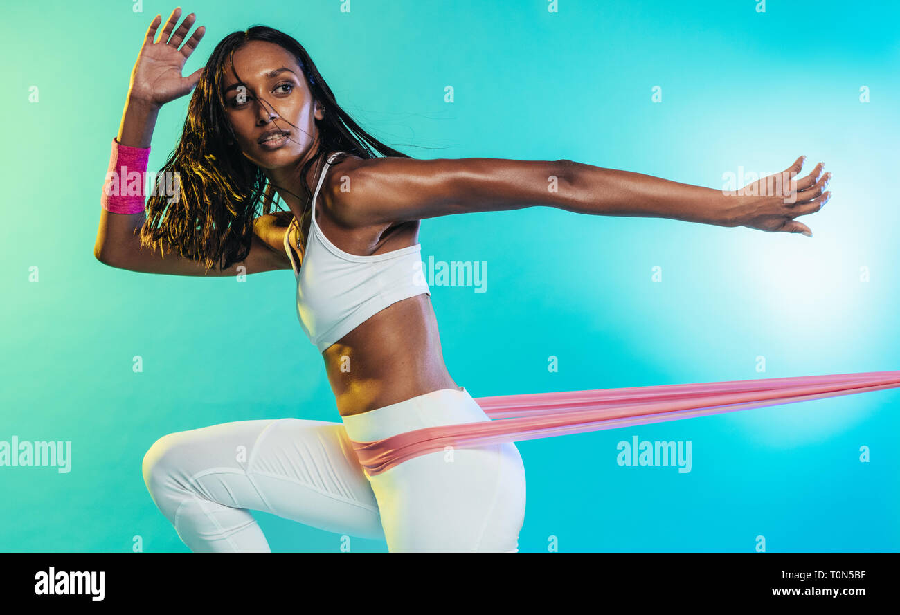 Starke junge Frau, die Übungen mit Widerstandsband über farbigem Hintergrund macht. Fitness-Frau, die mit Widerstandsband trainiert. Stockfoto