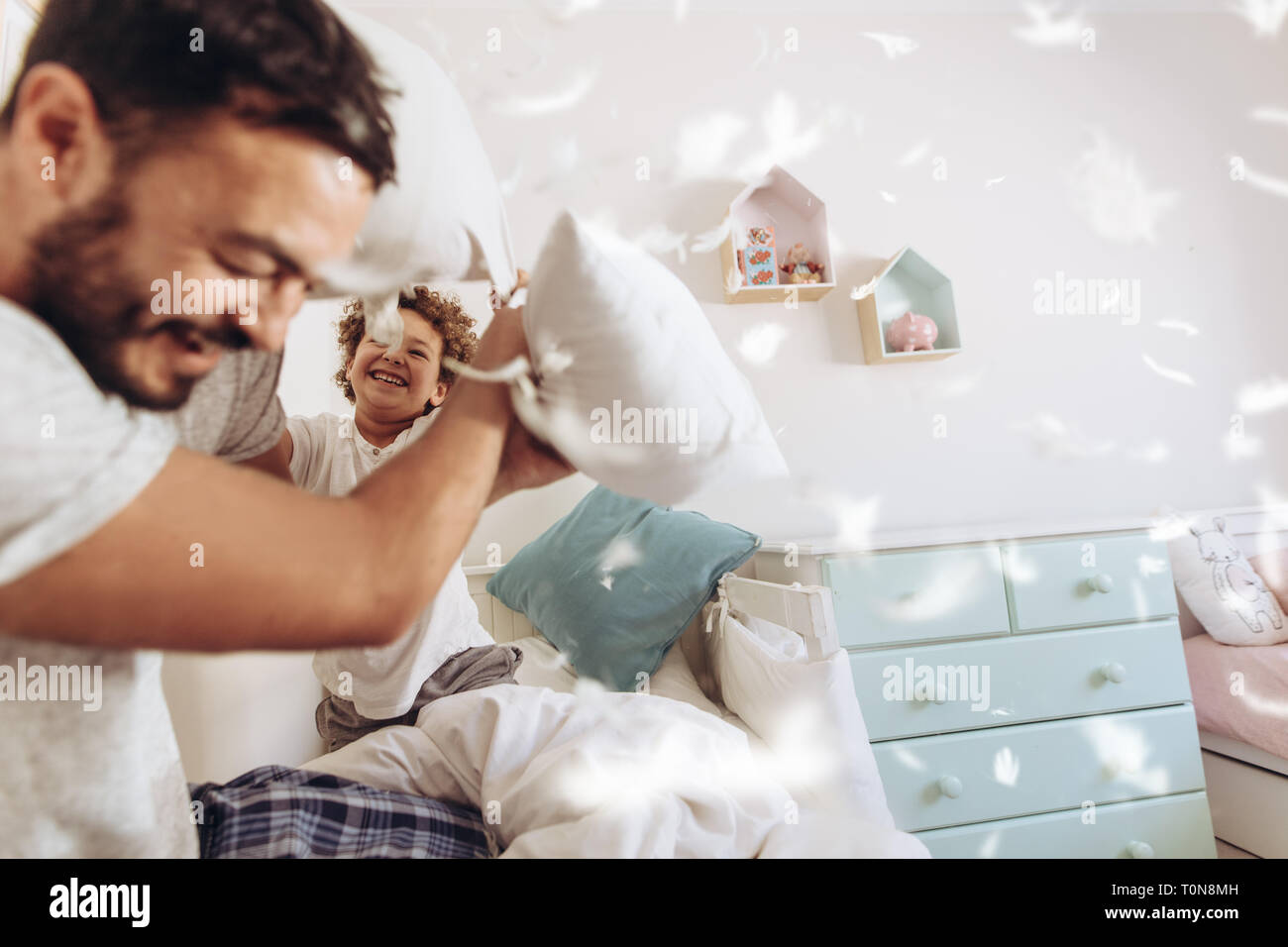 Fröhlicher mann Kissen mit Sohn sitzen auf dem Bett, zu Hause zu kämpfen. Vater und Sohn Spaß spielen mit Kopfkissen mit Federn fliegen herum. Stockfoto