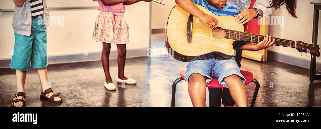 Lehrer, die Unterstützung einer Kinder zum spielen ein Musikinstrument im Klassenzimmer Stockfoto