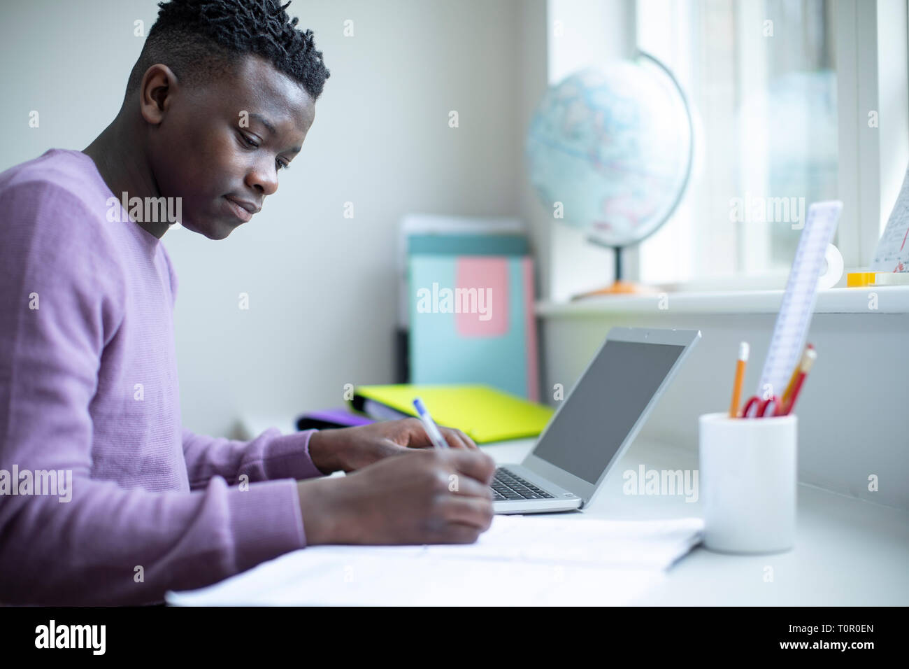 Teenager Junge sitzt am Schreibtisch tun Hausaufgabe auf Laptop Stockfoto