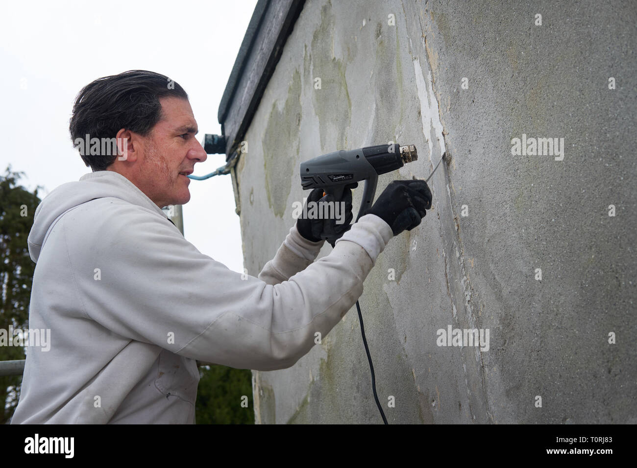 Baumeister, Maler und Dekorateur mit einer Heißluftpistole arbeiten an der Wand eines Hauses. Stockfoto