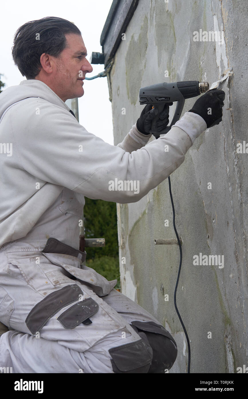 Baumeister, Maler und Dekorateur mit einer Heißluftpistole arbeiten an der Wand eines Hauses. Stockfoto