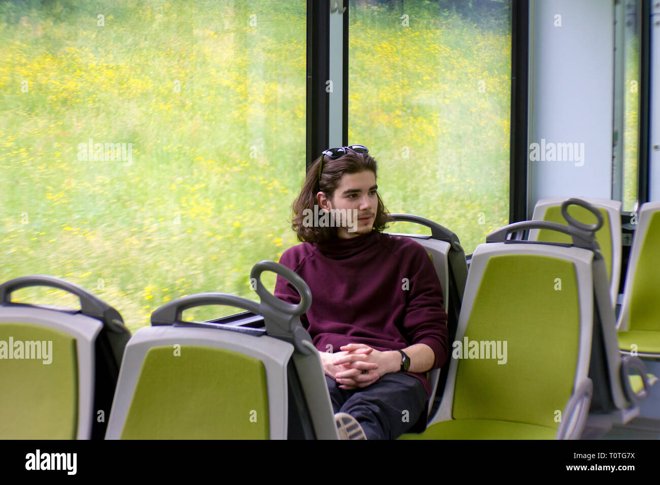 Ein hübscher Kerl fährt eine S-Bahn, sitzt und schaut aus dem Fenster, draußen vor dem Fenster ist eine blühende Frühlingswiese. Stockfoto