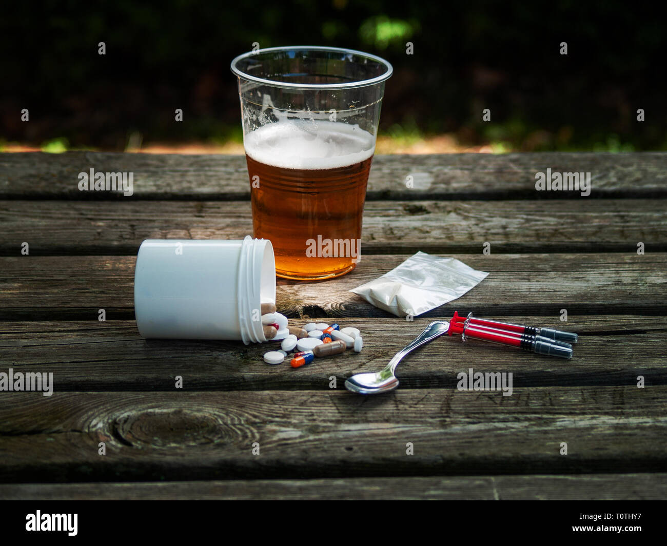 Ein Glas Bier, Pillen, Barbiturate, Drogen, Kokain, Heroin, eine Spritze  und ein Löffel auf einen Tisch. Drogensucht Konzept Stockfotografie - Alamy