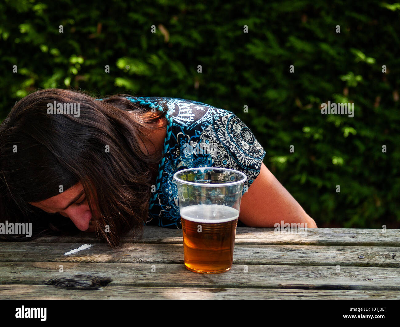 Eine Frau snorting eine Linie des Kokains auf einen hölzernen Tisch mit einem Glas Bier auf der Seite Stockfoto
