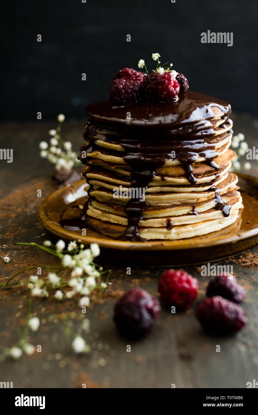 Stapel von Banana Pancakes gekrönt mit Schokolade Nieselregen und gefrorene Himbeeren Stockfoto