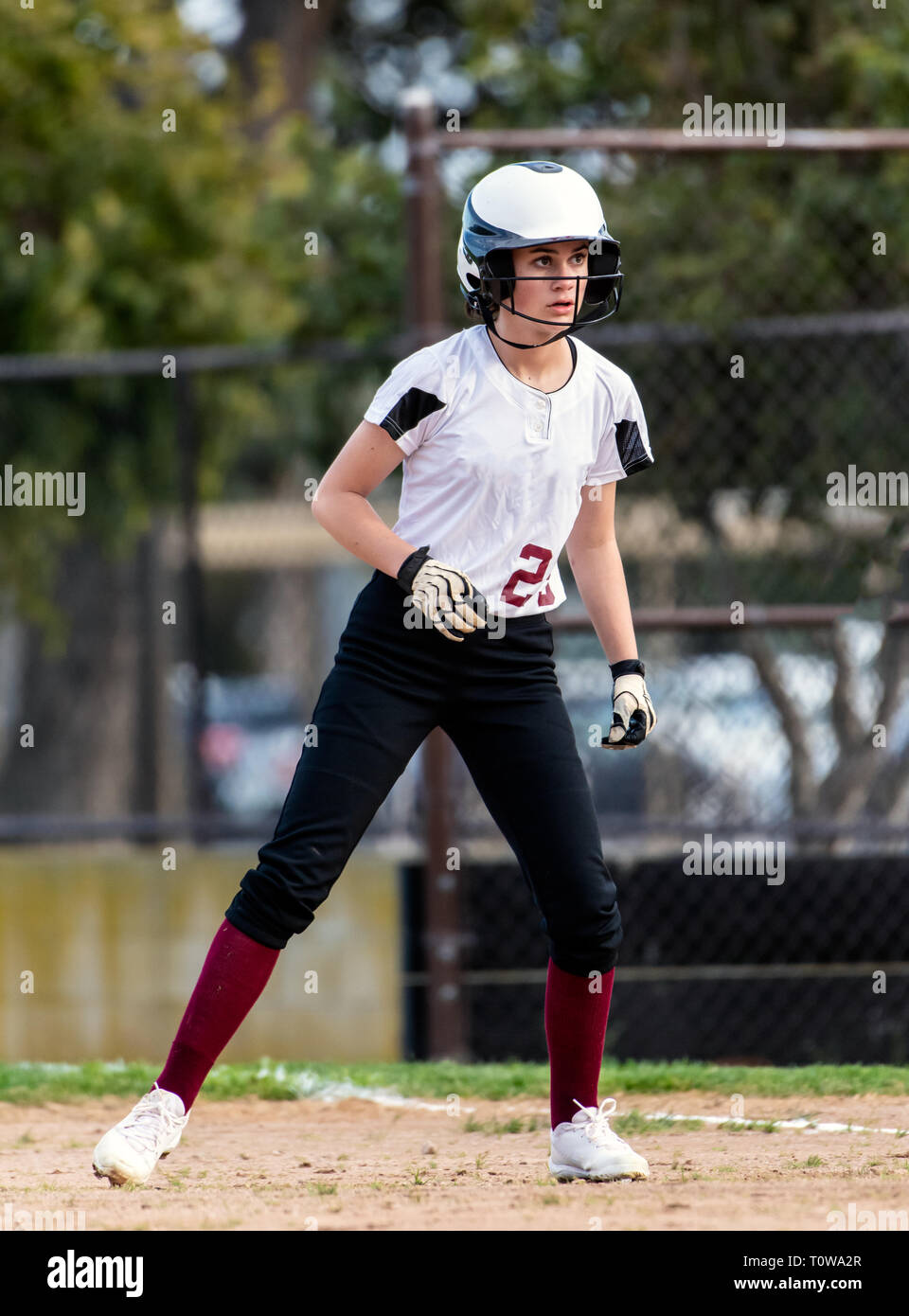 Weibliche jugendlich Softball Spieler in Schwarz und weiße Uniform, eine vorsichtige Führen weg von der ersten Base. Stockfoto