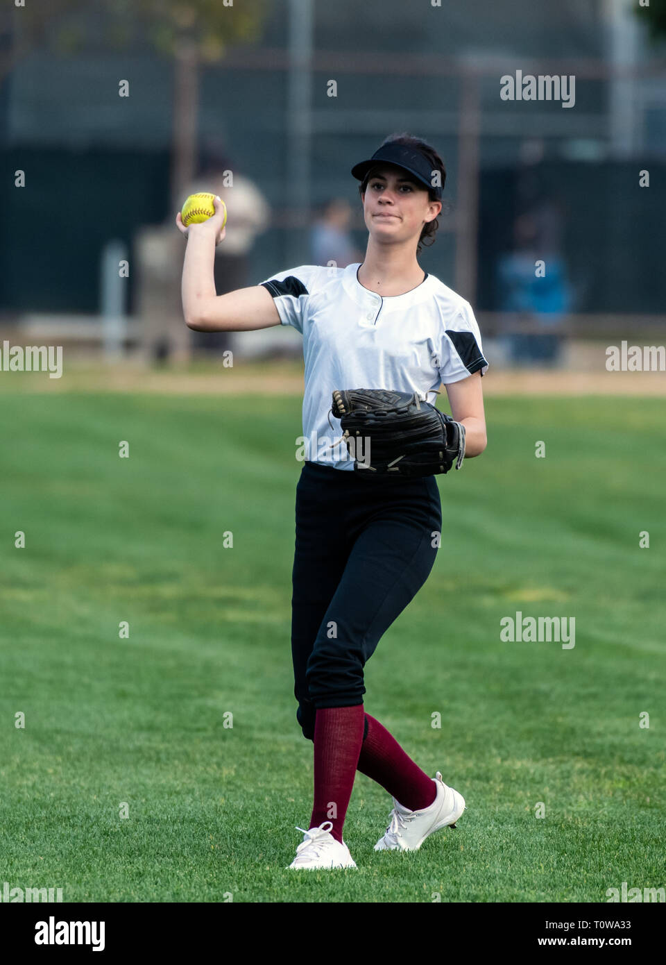 Weibliche jugendlich Softball Spieler in Schwarz und Weiß einheitliche Vorbereitung der Kugel auf dem outfield Gras zu werfen. Stockfoto
