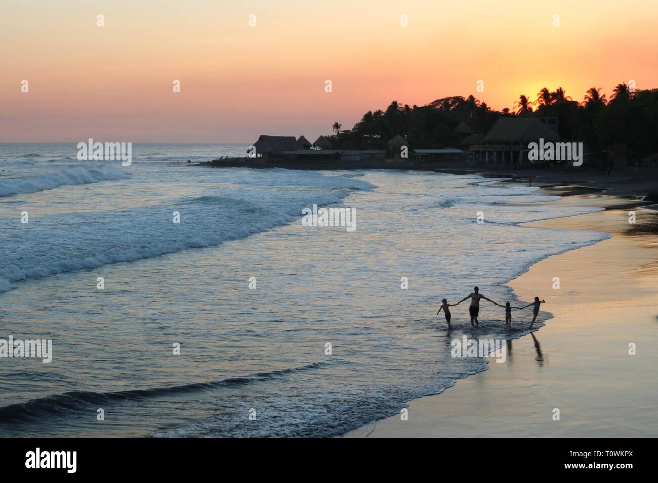 Silhouette von Vater und drei Kinder zu Fuß in die Brandung bei Sonnenuntergang an einem tropischen Strand in El Salvador Stockfoto