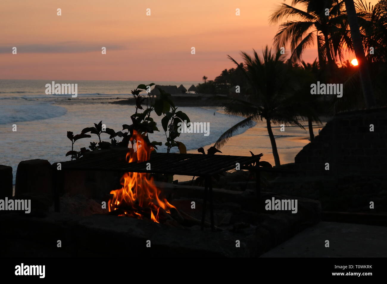 Orange Sonnenuntergang an einem tropischen Strand mit einem kleinen Feuer in El Salvador Stockfoto