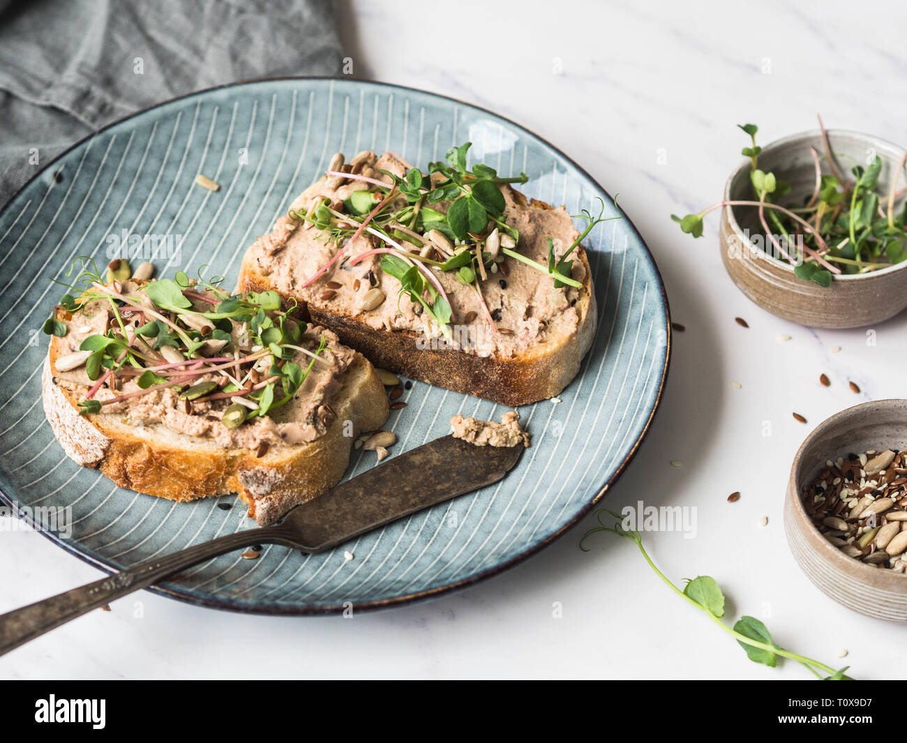 Zwei Toast Ente mit Backpflaumen rillettes Pastete auf Weißbrot mit Sprossen und verschiedenen Samen auf einem blauen Platte auf weißem Hintergrund Stockfoto