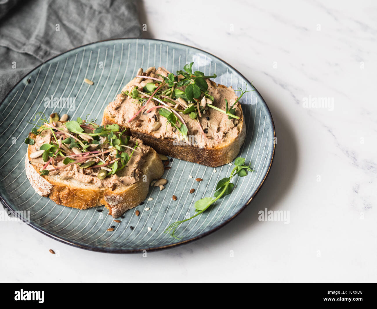 Zwei Toast Ente mit Backpflaumen rillettes Pastete auf Weißbrot mit Sprossen und verschiedenen Samen auf einem blauen Platte auf weißem Hintergrund Stockfoto