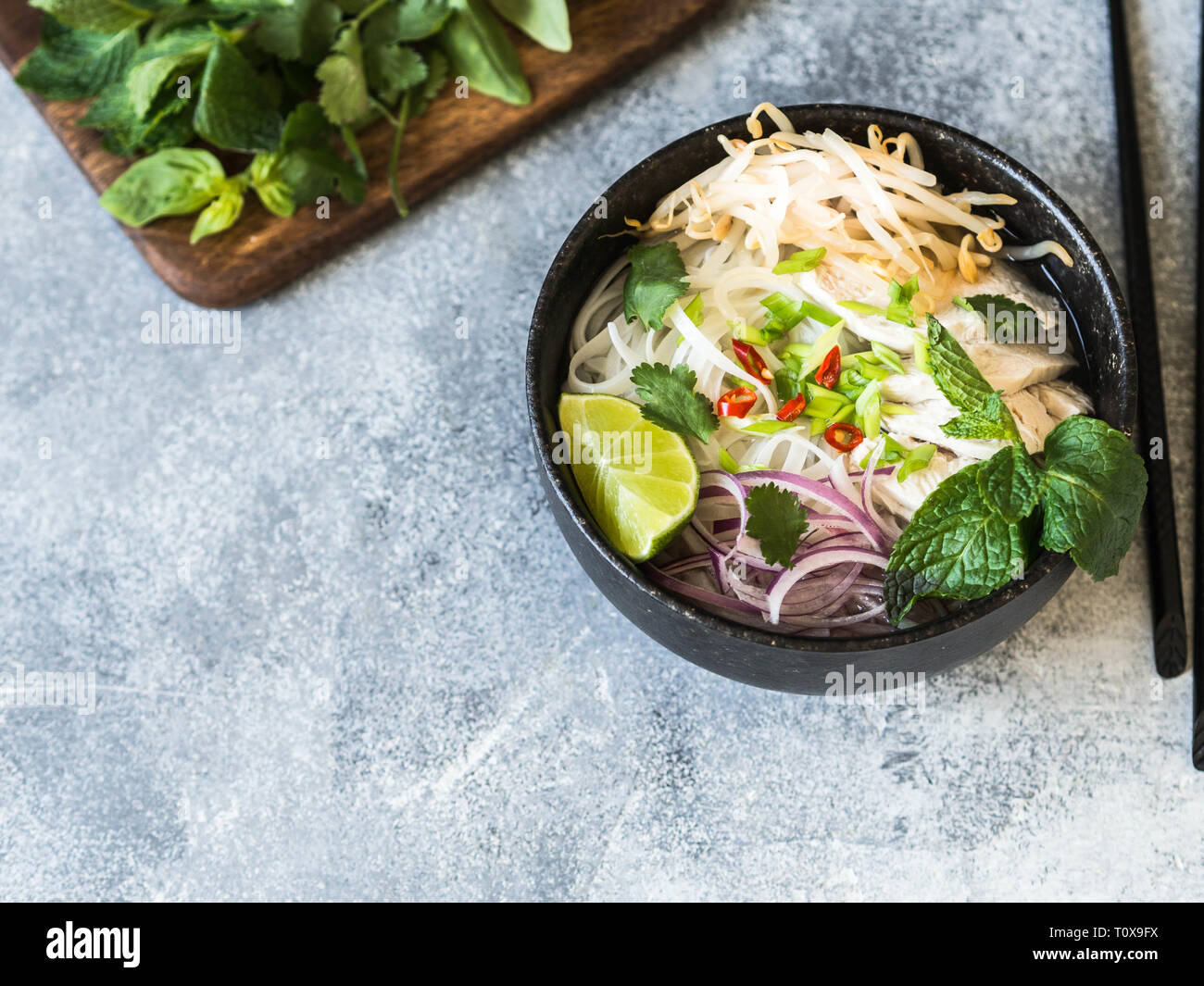 Traditionelle vietnamesische Suppe-Pho Ga in schwarz Schüssel mit Huhn und Reis Nudeln, Minze und cilantro, grüne und rote Zwiebel, Paprika, Sojasprossen und Kalk Stockfoto