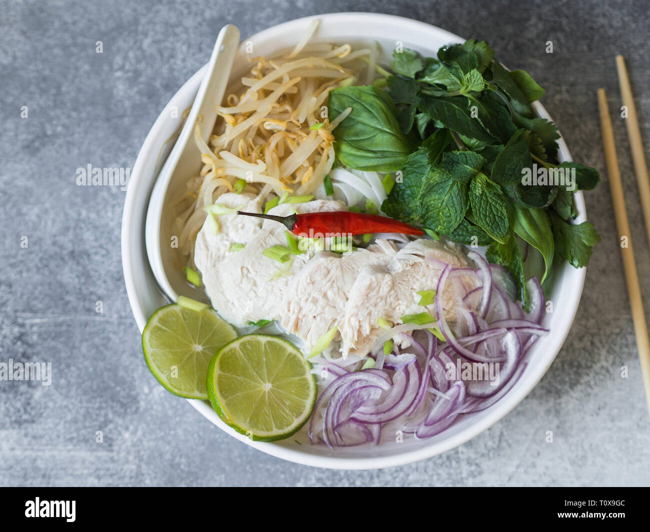Traditionelle vietnamesische Suppe-Pho Ga in weiße Schüssel mit Huhn und Reis Nudeln, Minze und cilantro, grüne und rote Zwiebel, Paprika, Sojasprossen und Kalk Stockfoto
