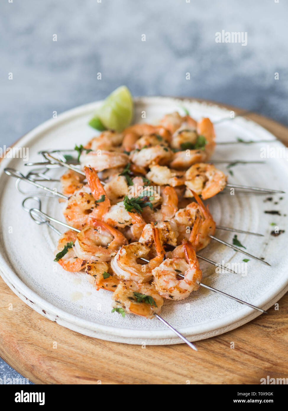 Gegrillte pikante Garnelen auf Metall Spieße mit Petersilie und Limettensaft auf weiße Platte Stockfoto