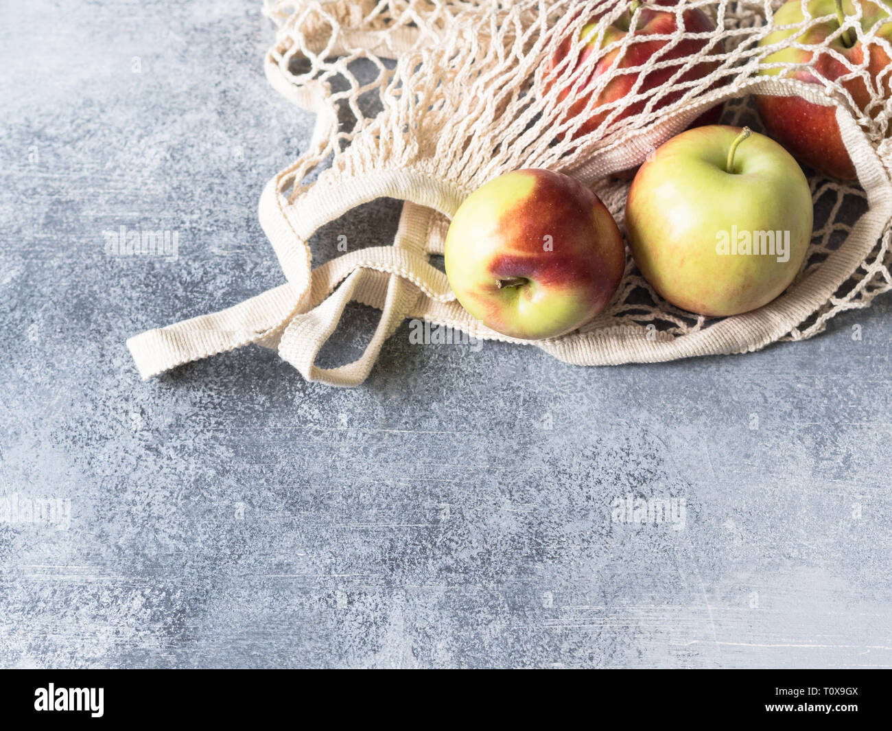 Umweltfreundliche beige Einkaufstasche mit roten Äpfeln auf grauem Hintergrund. String Beutel mit Früchten. Null Abfall, kein Plastik Konzept. Stockfoto