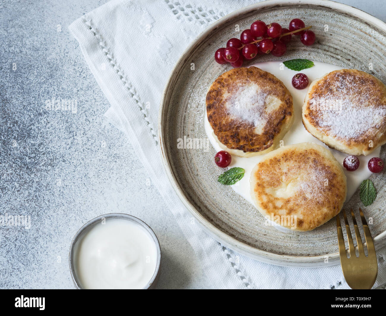 Hausgemachten Käse Kuchen aus Quark serviert auf einem weißen Keramikplatte mit Minze, Sauerrahm und Rote Johannisbeere auf grauem Hintergrund. Stockfoto