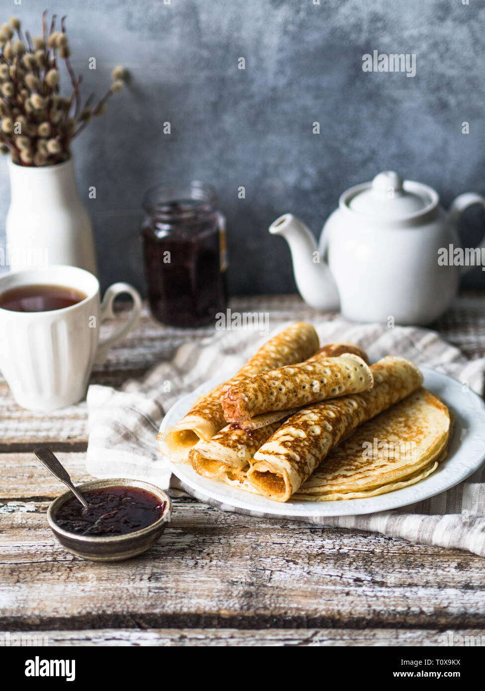 Russische hausgemachter Hefe Pfannkuchen gerollt in einem Rohr auf weiße Platte, Marmelade und Tee in die Tasse auf den Tisch. Traditionellen Weizen Pfannkuchen für Fastnacht. Stockfoto