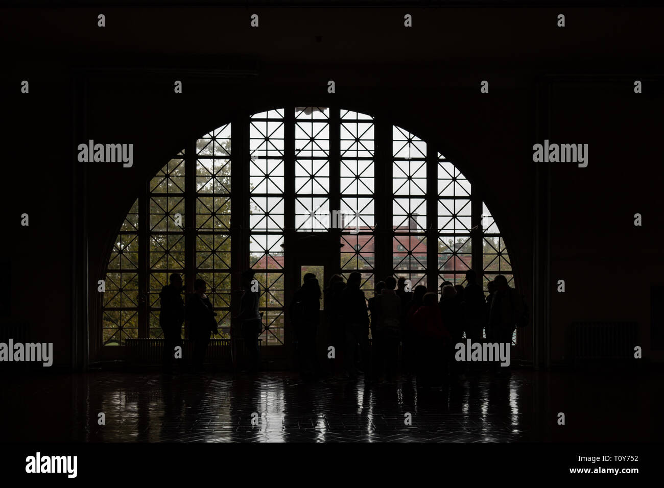 Touristen in Silhouette aus einem Halbkreis kunstvoll verglasten Fenster in der Registry Zimmer von Ellis Island in New York City. Stockfoto