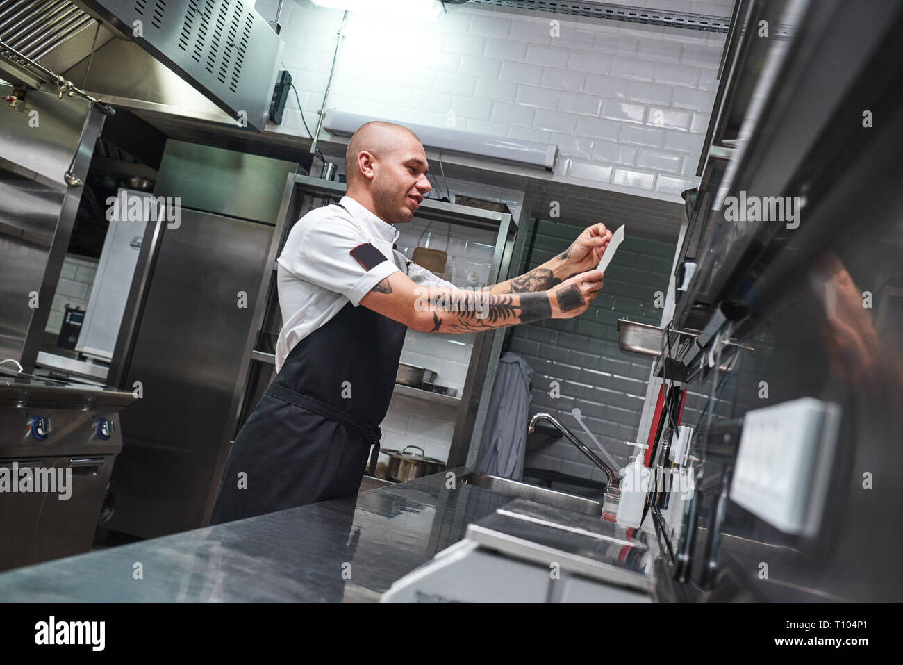 Was ist Weiter... Stattliche kahlen männlichen Chef mit Tattoos auf seine Arme auf der Liste in einem Restaurant Küche. Kochen Konzept Stockfoto