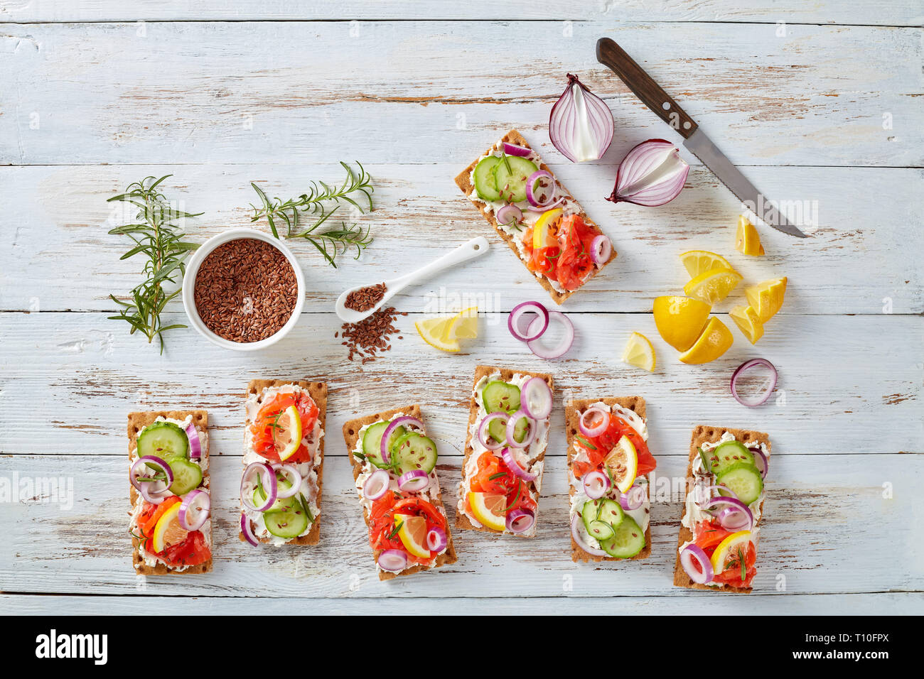 Dünne Sauerteig Roggen Knäckebrot lachs Sandwiches mit Gurke, Frischkäse und roten Zwiebeln, bestreut mit Leinsamen auf einem weißen alten Holztisch Stockfoto