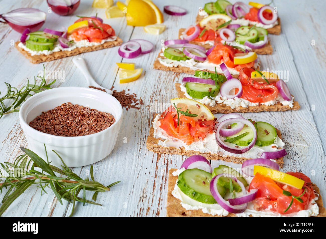 Knäckebrot Open-faced Sandwich mit geräucherter Forelle, weiche Creme Käse, Gurken, rote Zwiebel, bestreut mit Leinsamen auf einem weißen alten hölzernen Tisch, schließen Stockfoto
