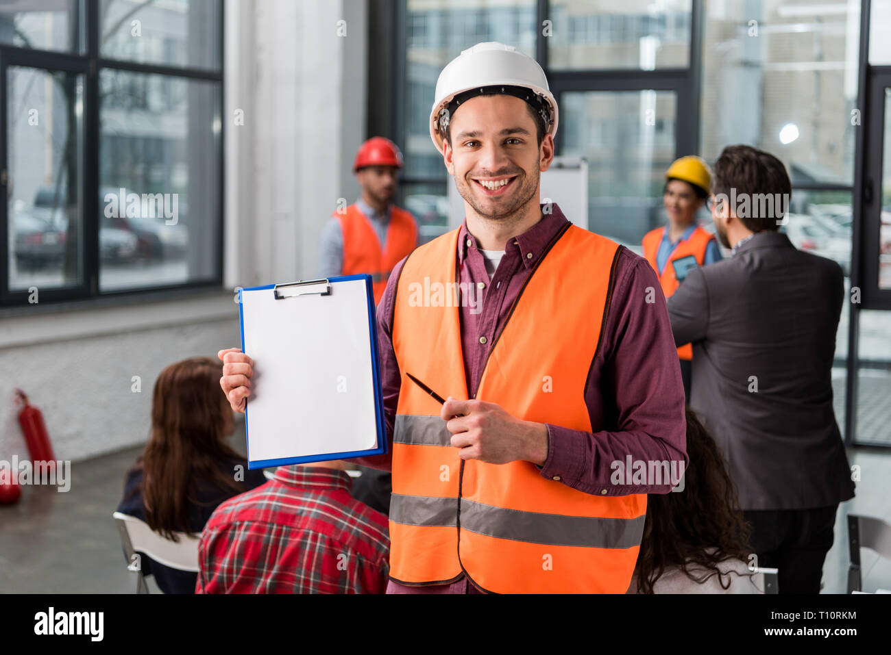 Selektiver Fokus der fröhlichen Feuerwehrmann auf Leere Zwischenablage zeigt mit Stift in der Nähe von Kollegen geben Sprechen auf Unterrichtung über den Hintergrund Stockfoto