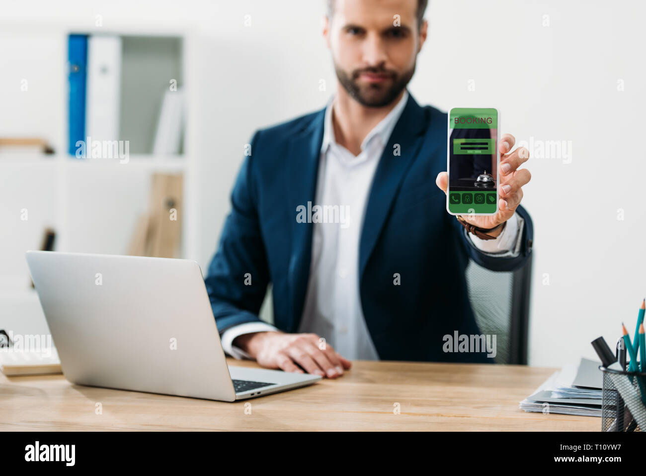 Selektiver Fokus der Geschäftsmann am Tisch mit Laptop und Smartphone mit Buchung App auf dem Bildschirm im Büro Stockfoto
