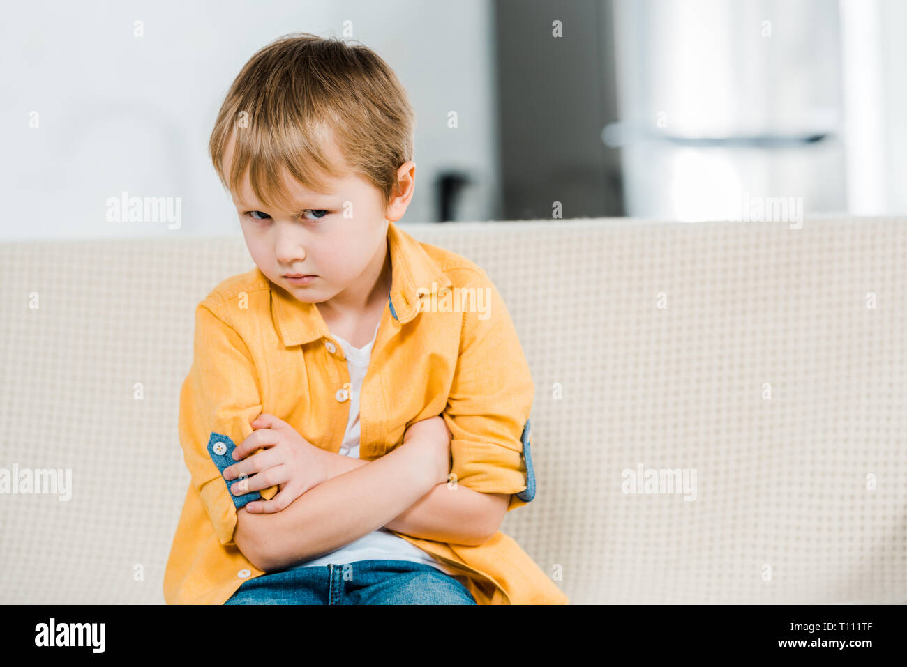 Unzufrieden Vorschüler Junge sitzt mit verschränkten Armen und Kamera zu Hause suchen Stockfoto