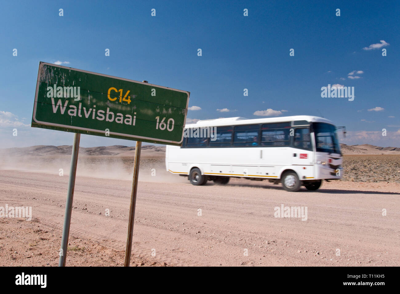 Ein Bus fährt durch ein Schild auf der Schotterstraße zwischen Walvis Bay und die Dünen bei Sossusvlei im Namib-Naukluft-Nationalpark, Namibia. Stockfoto