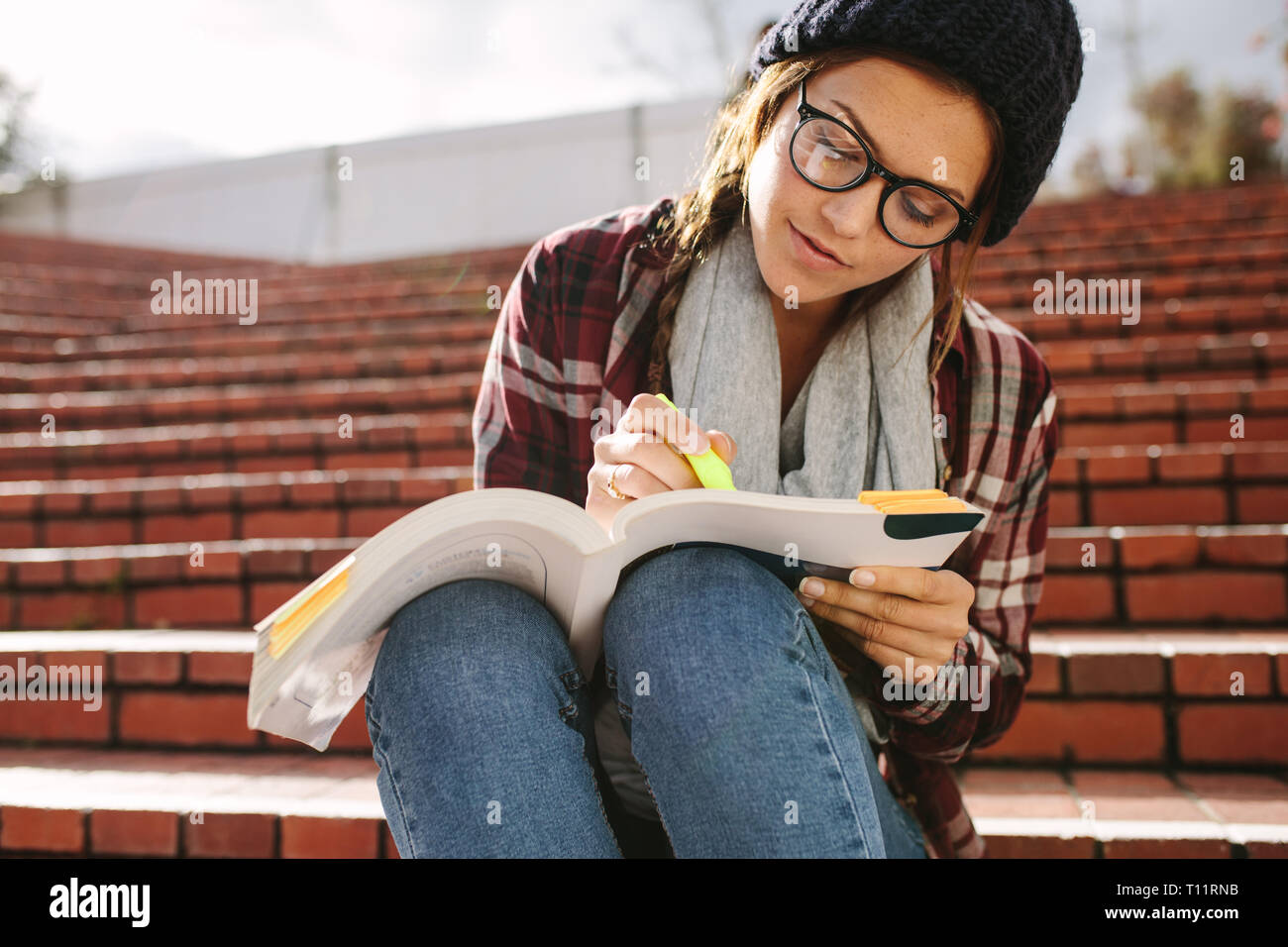 Studentin mit Marker Text in einem Buch zu markieren. Studentin auf Schritte auf dem Campus sitzen und Studieren. Stockfoto