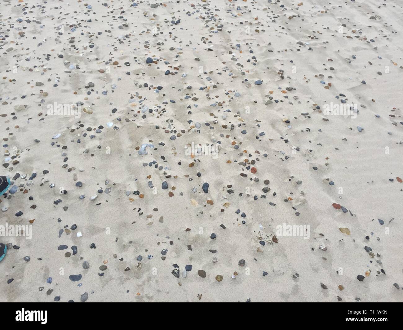 Eine Menge Steine, die im Sand verschwinden, so wie es von der Strum entfernt Stockfoto