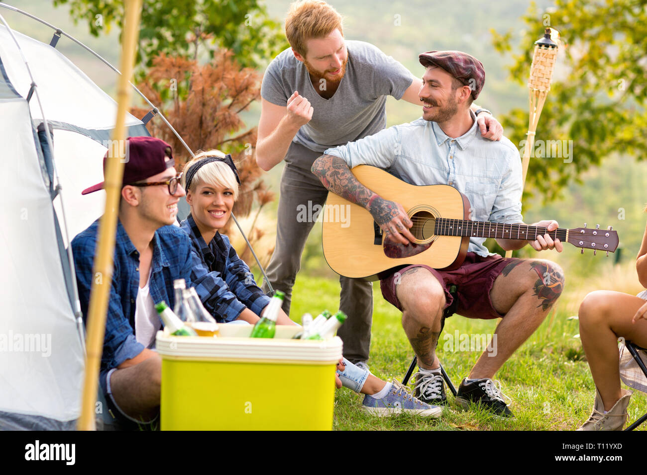 Tätowiert Kerl Gitarre spielen, Singen und Lachen mit Freunden vor dem Zelt in der Natur Stockfoto
