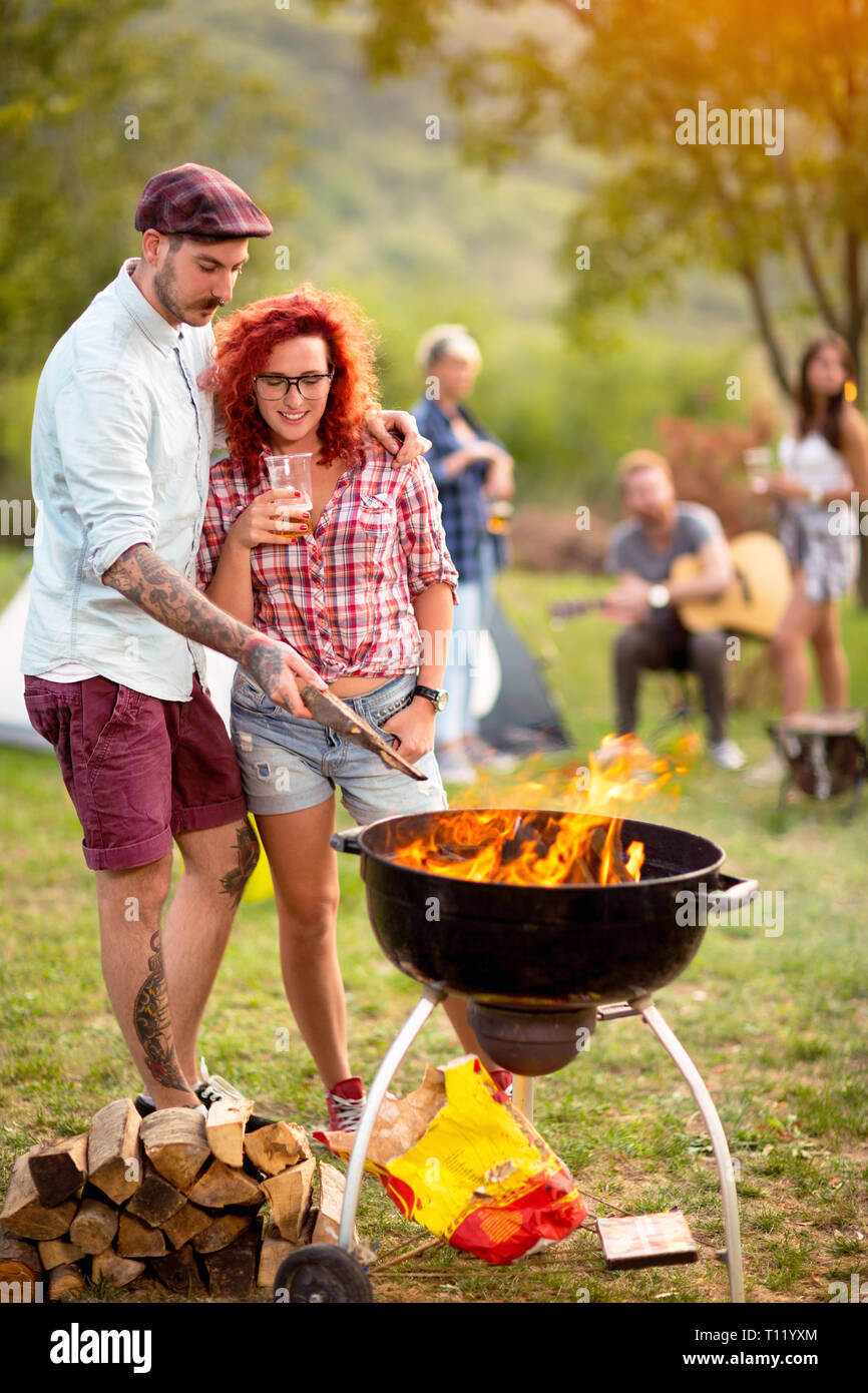 Curly Ingwer Mädchen mit tätowierten Kerl suchen im Grill Feuer im Camp in der Natur Stockfoto