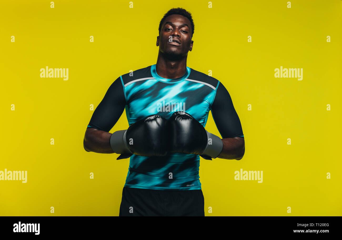Afrikanischer Mann in Sportkleidung mit Boxhandschuhen an Kamera gegen den gelben Hintergrund. Passen junge männliche Boxer. Stockfoto